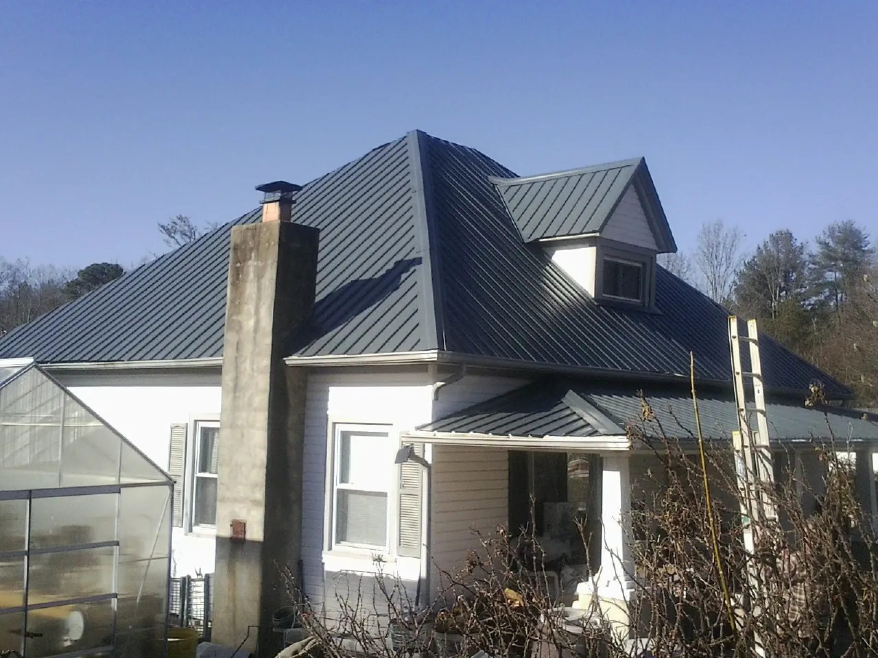 Dark blue standing seam metal roof on a white farmhouse with dormer — Slate & Tile Roof Repair by Roofing Brothers in Cudahy