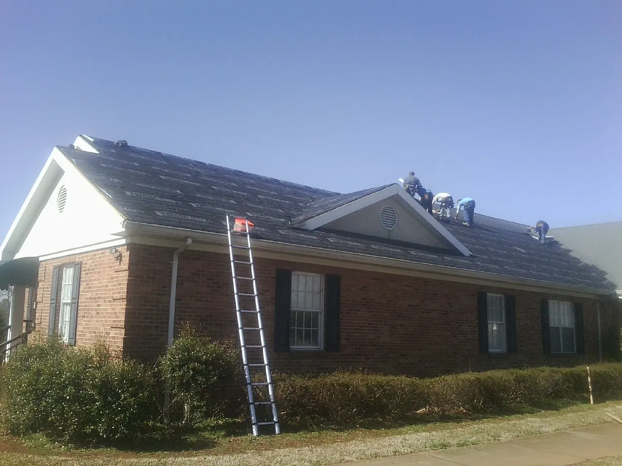 Crew tearing shingles off a brick ranch roof with a ladder set — Emergency Roof Repair work by our crew in Cudahy