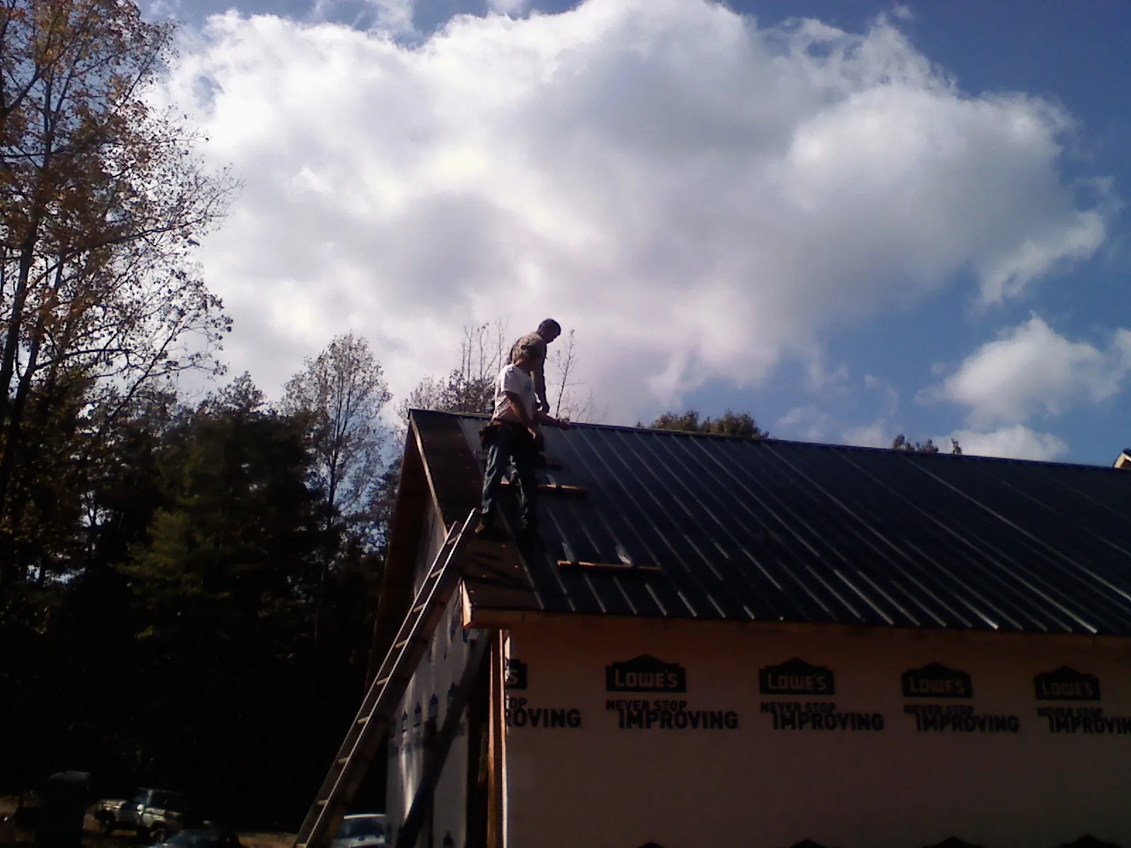 Roofer fastening dark metal panels high against a cloudy sky, from a Roof Inspection job in Cudahy