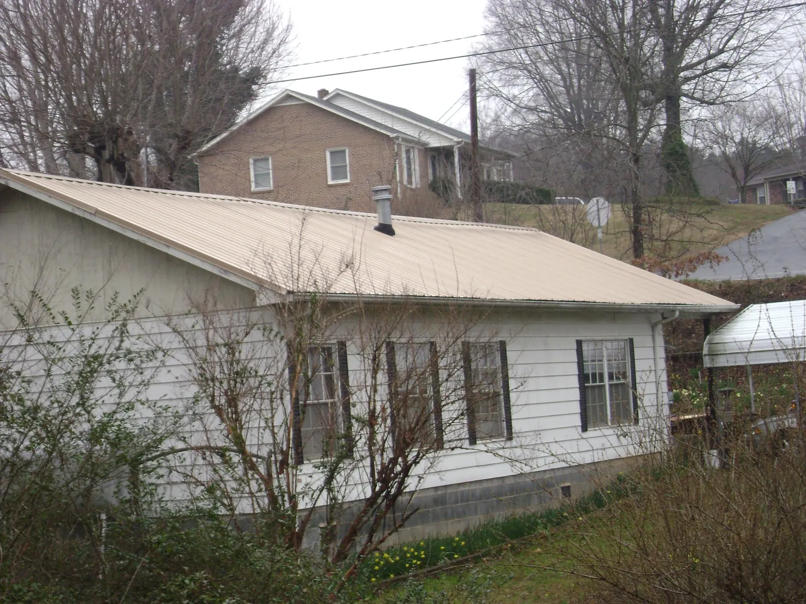 Tan metal roof on a white sided house set into a hillside — Commercial Roofing by Roofing Brothers in Cudahy